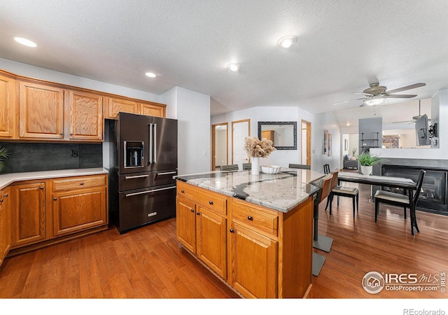 kitchen with light stone countertops, light hardwood / wood-style flooring, high quality fridge, and a kitchen island