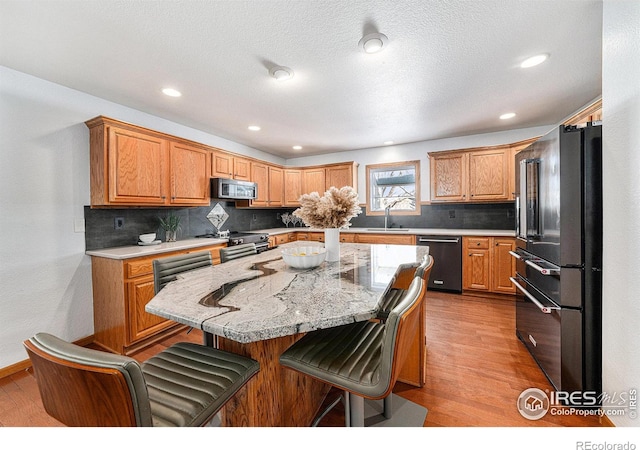 kitchen with a breakfast bar, stainless steel appliances, a center island, light stone counters, and light wood-type flooring