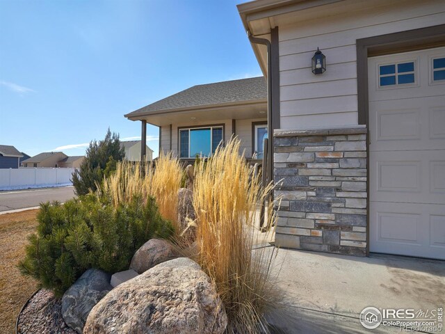 property entrance with a garage, stone siding, a shingled roof, and fence