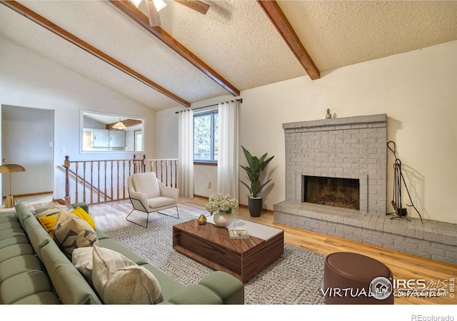 living room with vaulted ceiling with beams, hardwood / wood-style flooring, ceiling fan, a brick fireplace, and a textured ceiling