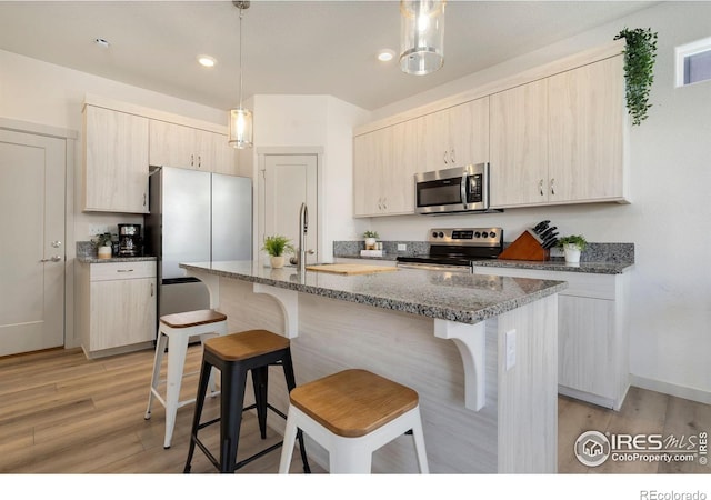 kitchen with a kitchen island with sink, decorative light fixtures, stone countertops, and appliances with stainless steel finishes