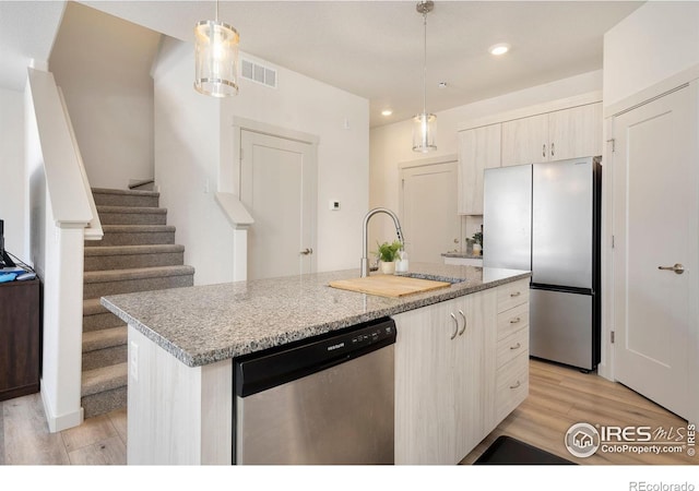 kitchen with stainless steel appliances, sink, hanging light fixtures, and a center island with sink