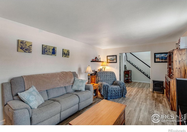 living room featuring a wood stove, baseboards, light wood finished floors, and stairs