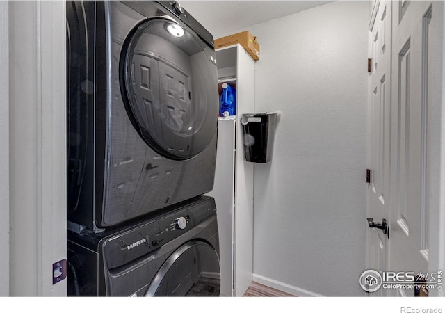 laundry room with laundry area, baseboards, stacked washing maching and dryer, and wood finished floors