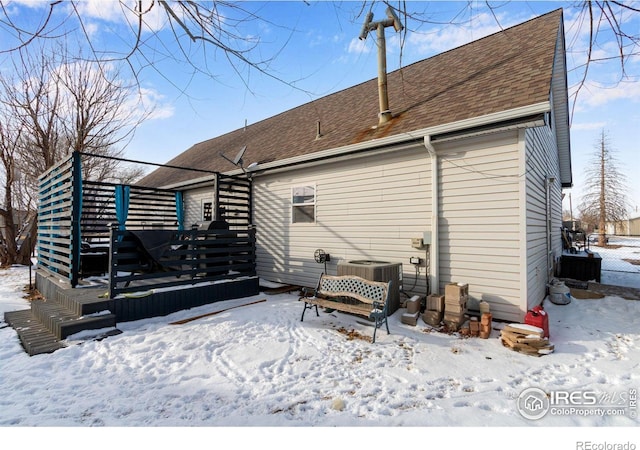 snow covered back of property featuring a deck, a shingled roof, and central air condition unit