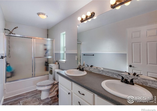 full bath featuring double vanity, shower / bath combination with glass door, a sink, and wood finished floors