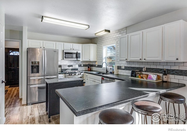 kitchen featuring a peninsula, a sink, appliances with stainless steel finishes, light wood finished floors, and dark countertops