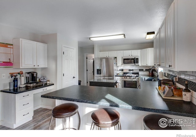 kitchen with a peninsula, stainless steel appliances, light wood-style floors, white cabinetry, and a sink