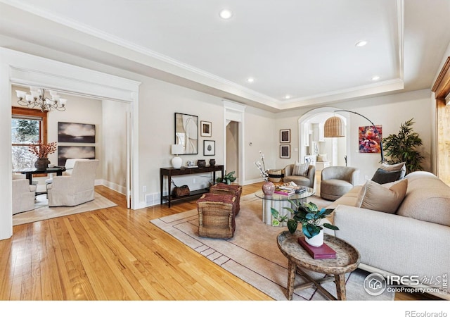 living room with hardwood / wood-style floors, crown molding, a notable chandelier, and a raised ceiling