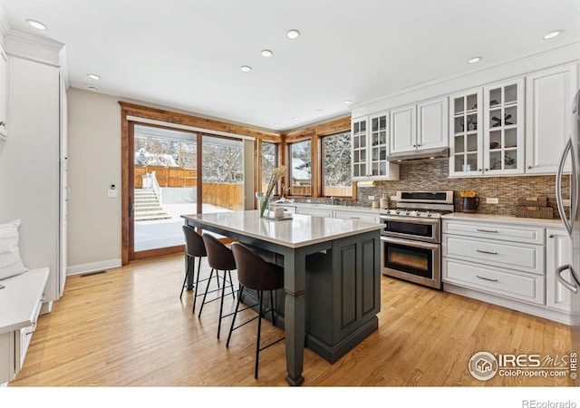 kitchen with white cabinetry, double oven range, backsplash, a kitchen breakfast bar, and a center island