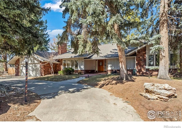 view of front of house with brick siding, driveway, a chimney, and a garage