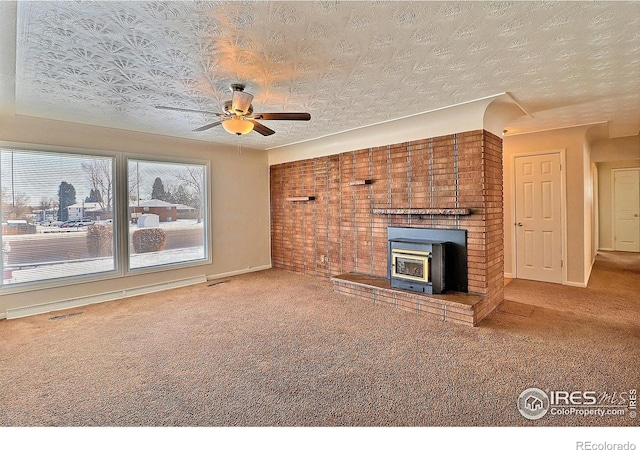 unfurnished living room with ceiling fan, carpet floors, a wood stove, and a textured ceiling