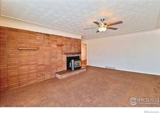 unfurnished living room featuring ceiling fan, a textured ceiling, carpet, and a wood stove