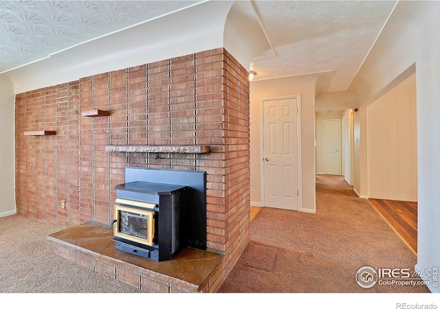 unfurnished living room featuring brick wall, carpet, a wood stove, and a textured ceiling