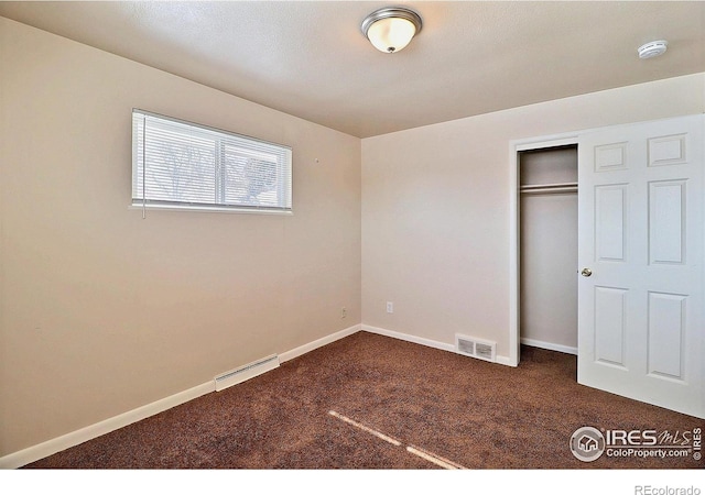 unfurnished bedroom with dark carpet and a closet