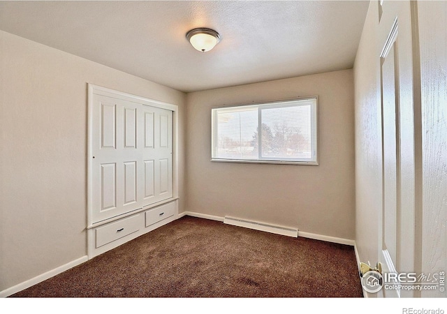 unfurnished bedroom with dark colored carpet and a baseboard heating unit