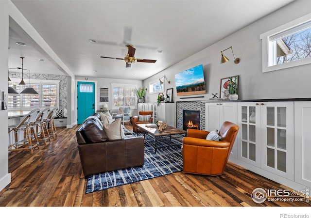 living room with ceiling fan, wood-type flooring, and a tiled fireplace