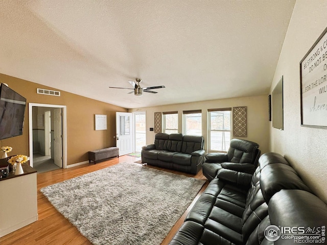 living room with light hardwood / wood-style flooring, ceiling fan, vaulted ceiling, and a textured ceiling