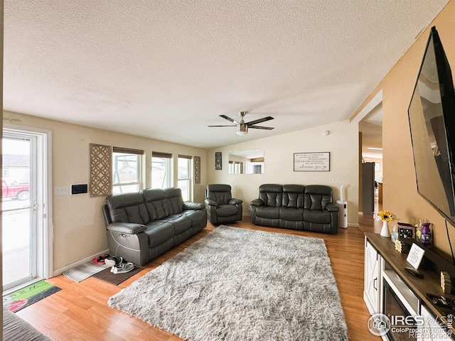 living room featuring ceiling fan, vaulted ceiling, light hardwood / wood-style flooring, and a textured ceiling