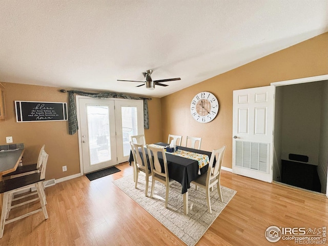 dining area with ceiling fan, lofted ceiling, light hardwood / wood-style floors, and a textured ceiling