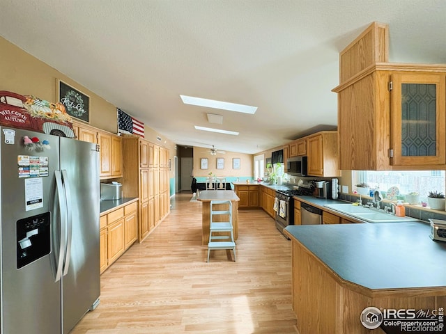 kitchen with a kitchen bar, sink, a center island, appliances with stainless steel finishes, and vaulted ceiling with skylight