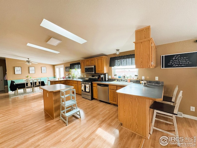 kitchen with sink, a breakfast bar, appliances with stainless steel finishes, vaulted ceiling, and kitchen peninsula