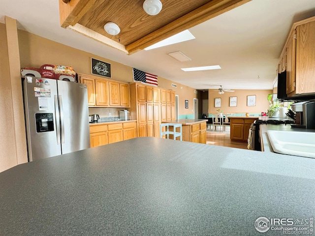 kitchen with a skylight, a center island, light brown cabinets, stainless steel fridge, and kitchen peninsula