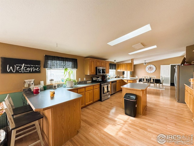 kitchen with lofted ceiling with skylight, a center island, appliances with stainless steel finishes, a kitchen breakfast bar, and light hardwood / wood-style floors