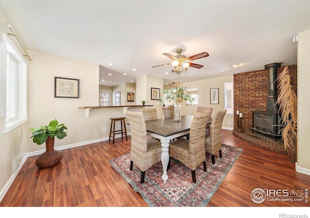 dining space with a wood stove, visible vents, baseboards, and wood finished floors