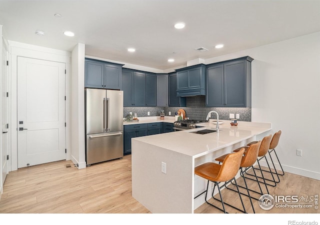 kitchen featuring high quality appliances, sink, a kitchen breakfast bar, light hardwood / wood-style floors, and kitchen peninsula