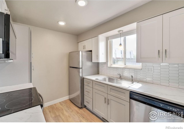 kitchen with light wood-style flooring, a sink, stainless steel appliances, white cabinetry, and backsplash