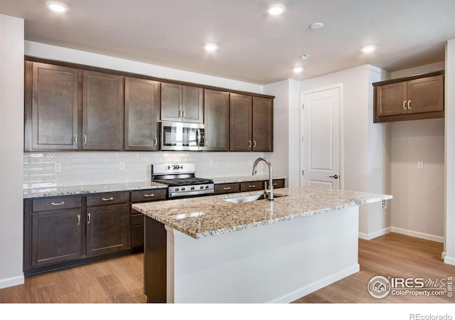 kitchen with light stone countertops, appliances with stainless steel finishes, sink, and a center island with sink