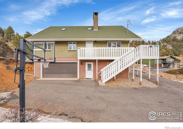 rear view of house with aphalt driveway, brick siding, a chimney, a garage, and stairs