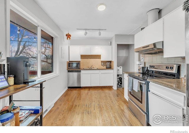 kitchen with stone counters, white cabinetry, range hood, stainless steel appliances, and light hardwood / wood-style floors