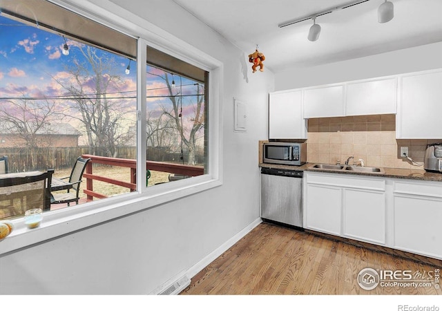 kitchen featuring tasteful backsplash, light hardwood / wood-style flooring, dark stone countertops, appliances with stainless steel finishes, and white cabinets