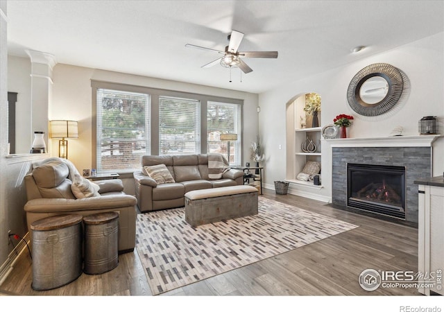 living room with built in shelves, ceiling fan, and wood-type flooring