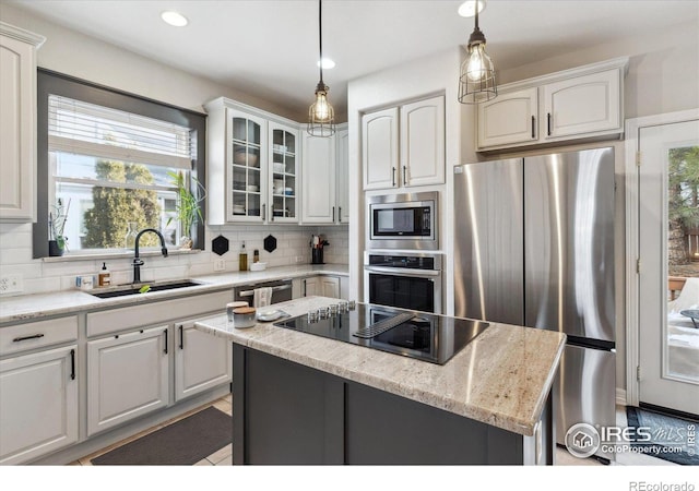 kitchen with appliances with stainless steel finishes, decorative light fixtures, white cabinetry, sink, and a center island