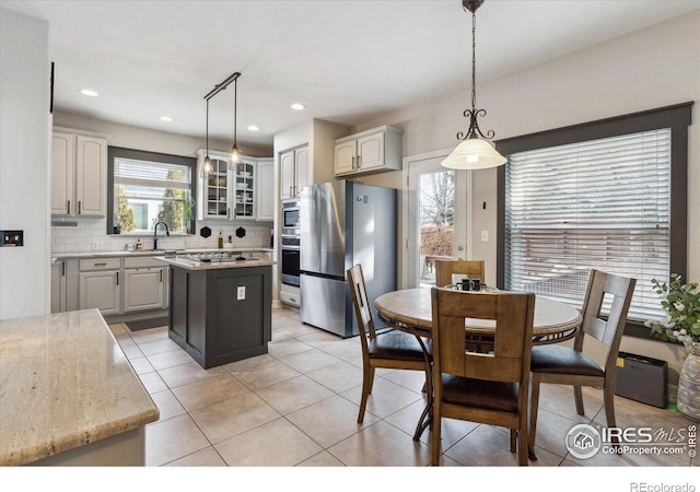 kitchen featuring sink, appliances with stainless steel finishes, backsplash, a center island, and decorative light fixtures