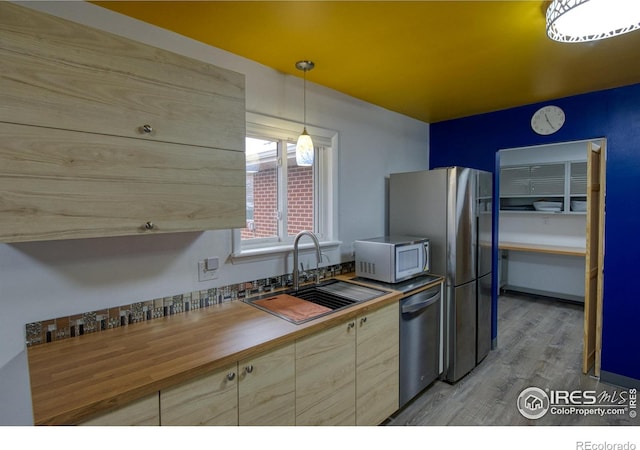 kitchen with sink, butcher block countertops, hanging light fixtures, stainless steel appliances, and light hardwood / wood-style floors