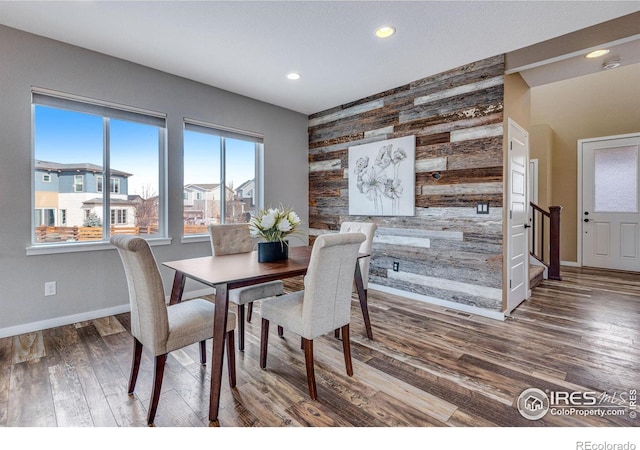 dining room with an accent wall, wood finished floors, stairs, wood walls, and recessed lighting