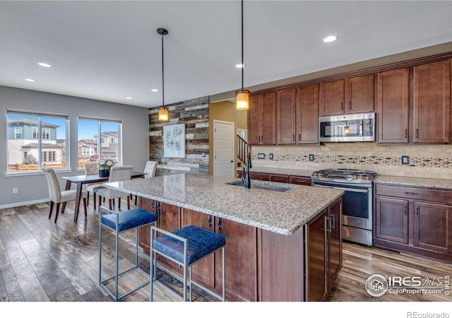 kitchen featuring stainless steel appliances, a sink, a kitchen breakfast bar, an island with sink, and decorative light fixtures