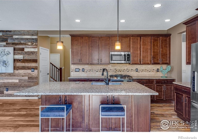 kitchen with stainless steel microwave, decorative light fixtures, and an island with sink
