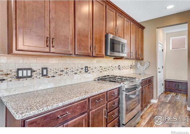 kitchen featuring dark wood finished floors, stainless steel appliances, decorative backsplash, light stone countertops, and baseboards