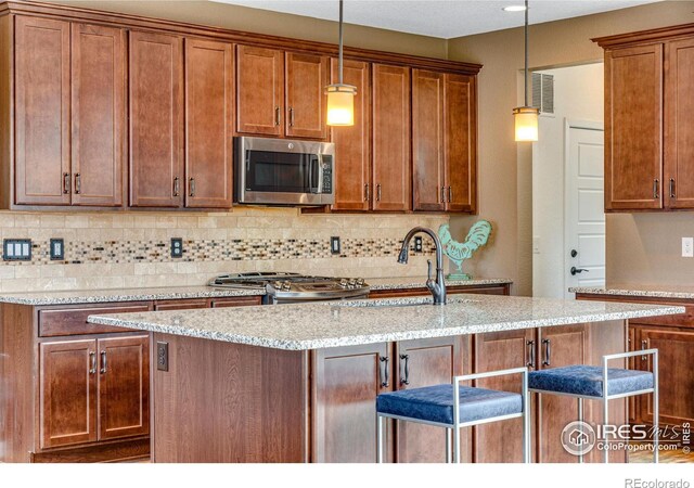 kitchen with hanging light fixtures, light stone countertops, appliances with stainless steel finishes, and brown cabinets