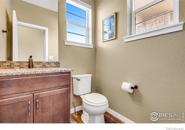 bathroom featuring baseboards, toilet, wood finished floors, vanity, and backsplash