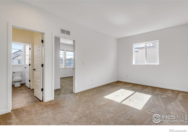 unfurnished bedroom featuring light carpet, visible vents, baseboards, and ensuite bathroom