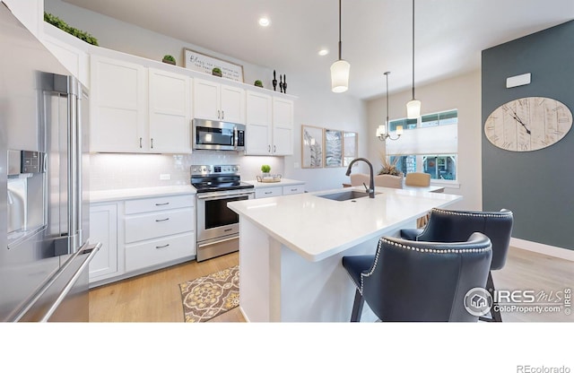 kitchen featuring a breakfast bar, sink, decorative light fixtures, appliances with stainless steel finishes, and white cabinets