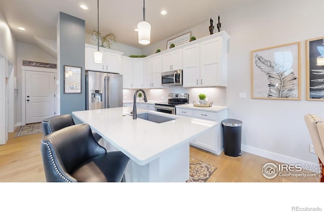 kitchen with decorative light fixtures, white cabinetry, sink, stainless steel appliances, and a center island with sink