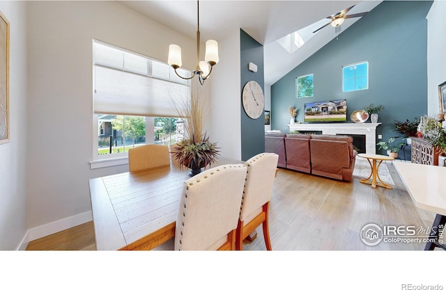 dining space featuring ceiling fan with notable chandelier, high vaulted ceiling, and light hardwood / wood-style floors