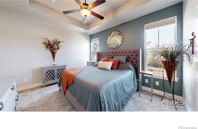 bedroom with ceiling fan, a tray ceiling, and light carpet